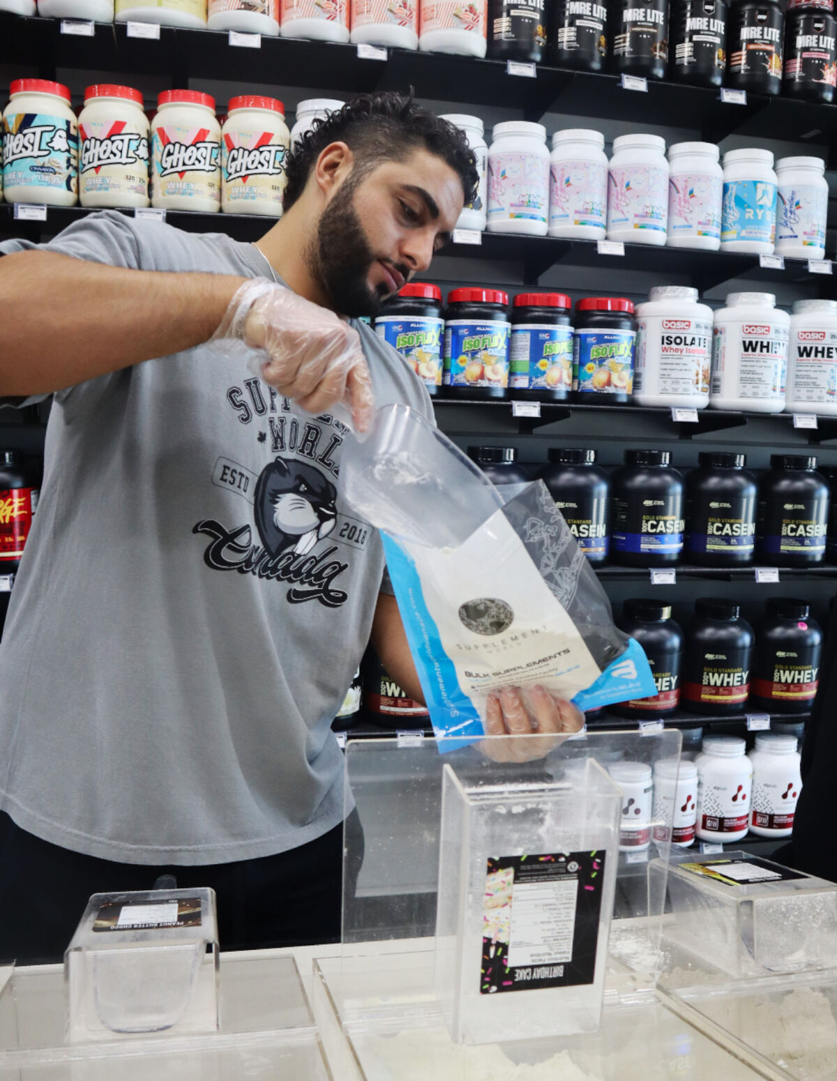 A Supplement World team member weighing bulk protein powder into a branded bulk supplements bag at the Newcastle store